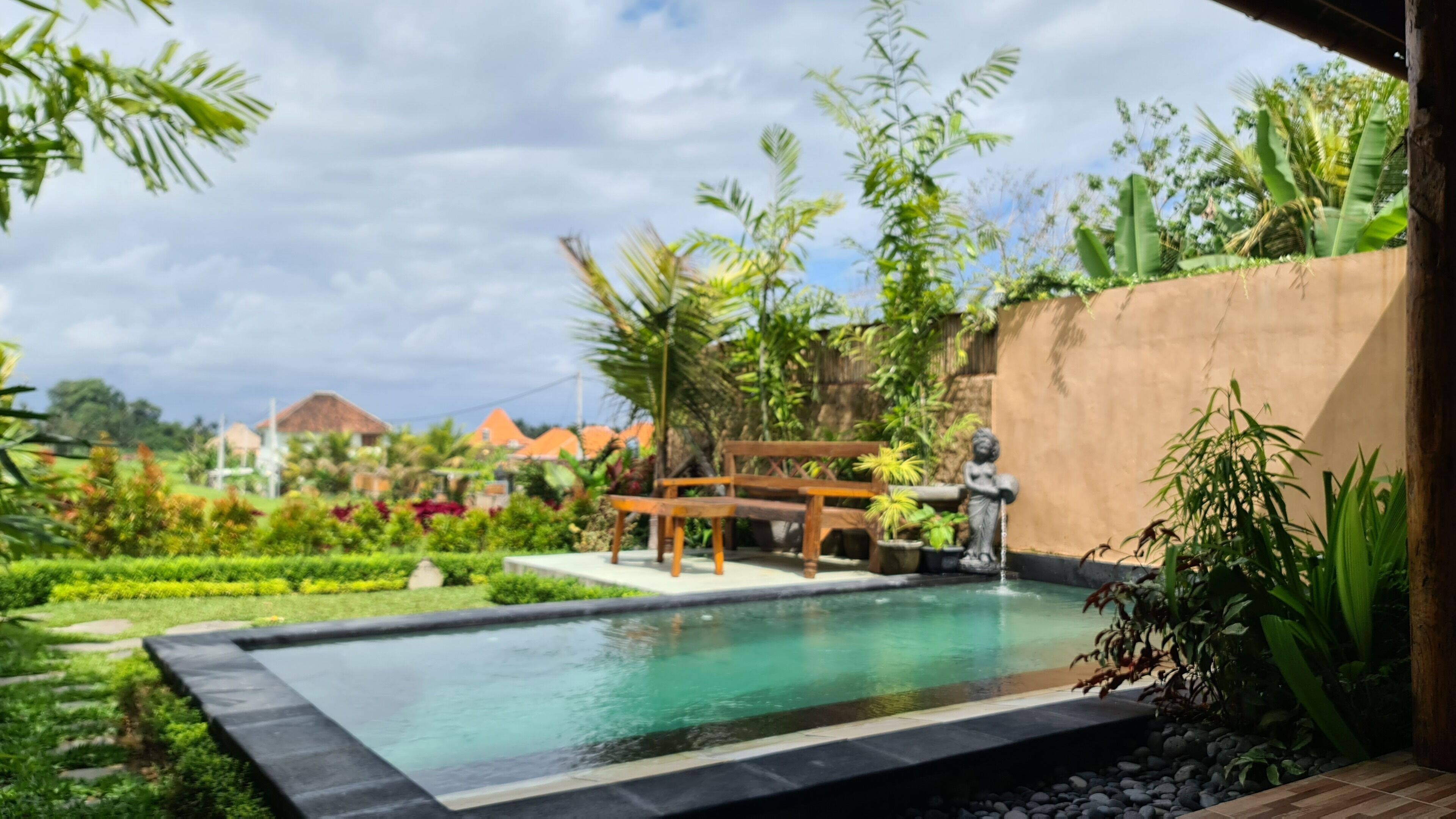 Une piscine dotée d’une terrasse en bois, entourée d’une végétation luxuriante et d’un mur de pierre.