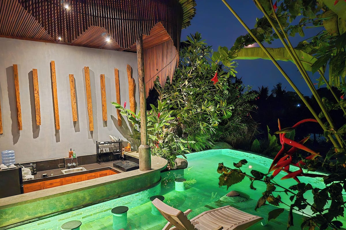 A pool area with lounge chairs, a bar, and a tropical plant arrangement.