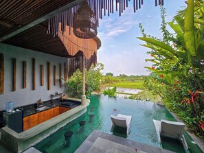 Piscina infinita con zona de bar, rodeada de exuberante vegetación y vista a un campo de arroz.