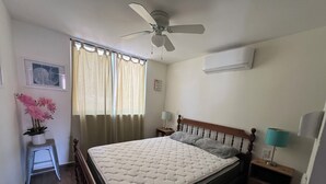 A bedroom with a bed, a ceiling fan, a window with curtains, a bedside table with a lamp, and an air conditioning unit. - 5 minutes walk to the town square. Gated Community condo w (Crucecita)