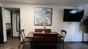 A dining area with a wooden table and chairs, a painting on the wall, a TV mounted on the wall, and a plant in the corner. - 5 minutes walk to the town square. Gated Community condo w (Crucecita)