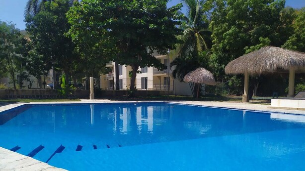 A swimming pool with clear blue water, surrounded by stone tiles. - 5 minutes walk to the town square. Gated Community condo w (Crucecita)