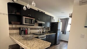 A modern kitchen with dark cabinets, a granite countertop, stainless steel appliances, and a central island with stools. - 5 minutes walk to the town square. Gated Community condo w (Crucecita)