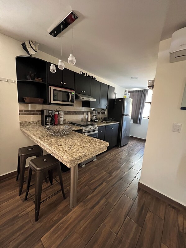 Una cocina moderna con armarios oscuros, encimera de granito, electrodomésticos de acero inoxidable y una isla central con taburetes.