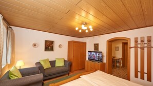 A cozy room with a wooden ceiling, a bed, a sofa, a TV, and a small dining area. - Ferienwohnung Hochries, 30 qm (Prien am Chiemsee)