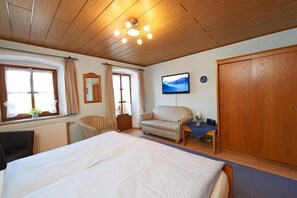 A bedroom with a large bed, a wooden wardrobe, a chair, and a television on the wall.