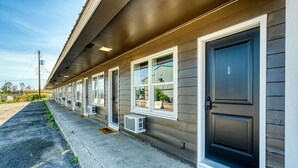 A row of motel rooms with individual air conditioning units, a dark-colored exterior, and a welcome mat at the entrance. - Comfy and Cozy Studio for 2 (101 Spring Creek) (Kalispell)