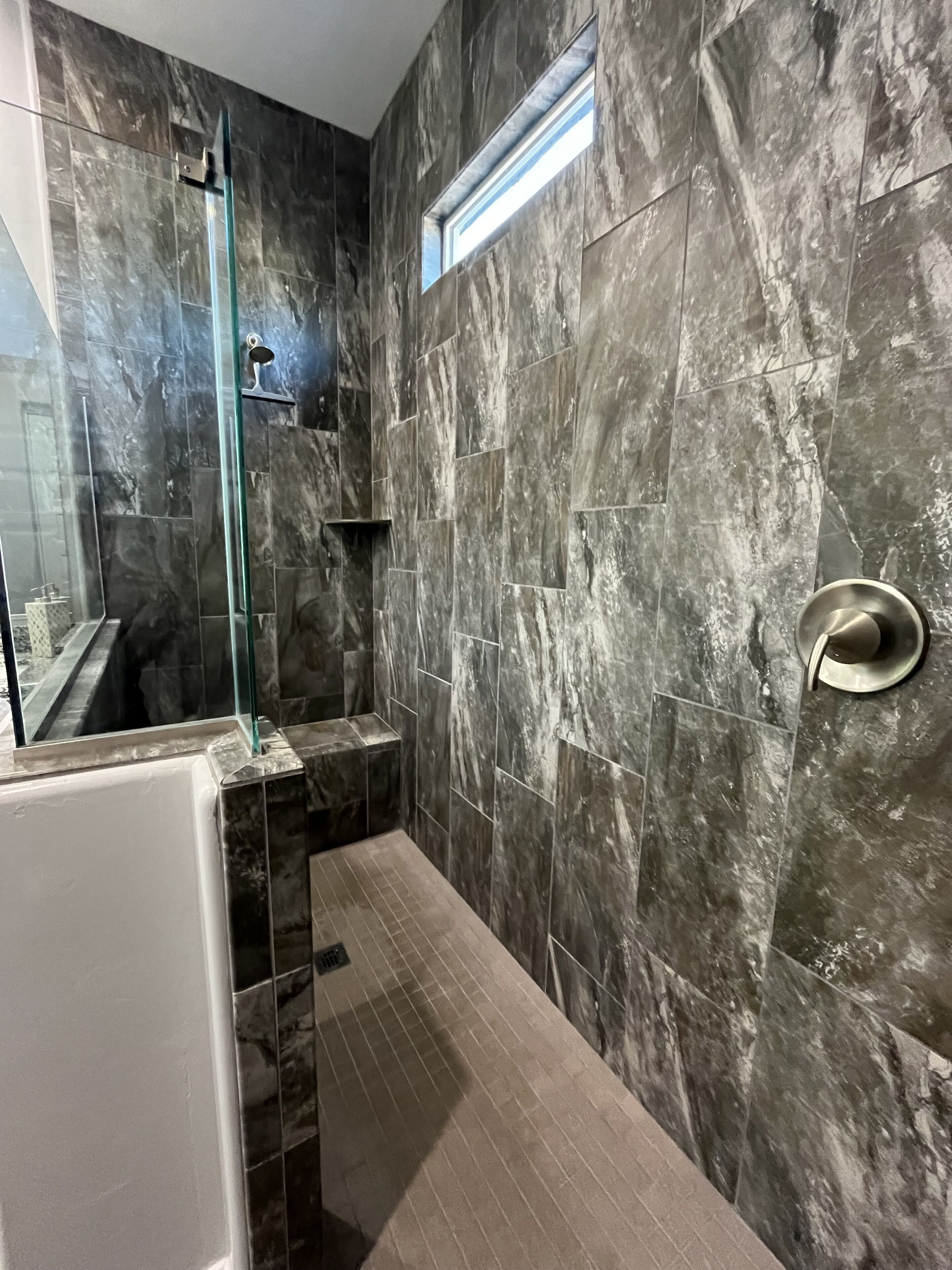 A modern bathroom with a glass shower enclosure, a bathtub, and a marble-tiled wall.