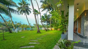 A lush garden with palm trees and a pathway leading to a building with a stone facade. - Kochi Backwater Resort (Ernakulam)