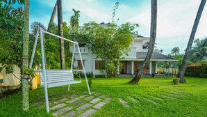 A white house with a porch, surrounded by lush greenery and palm trees. - Kochi Backwater Resort (Ernakulam)