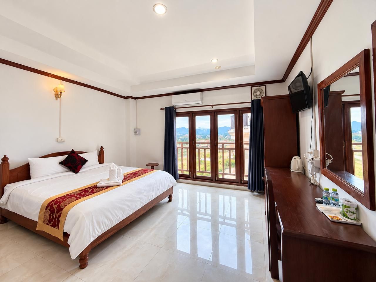 A hotel room with a large bed, a desk, a flat-screen TV, and a balcony with a view.