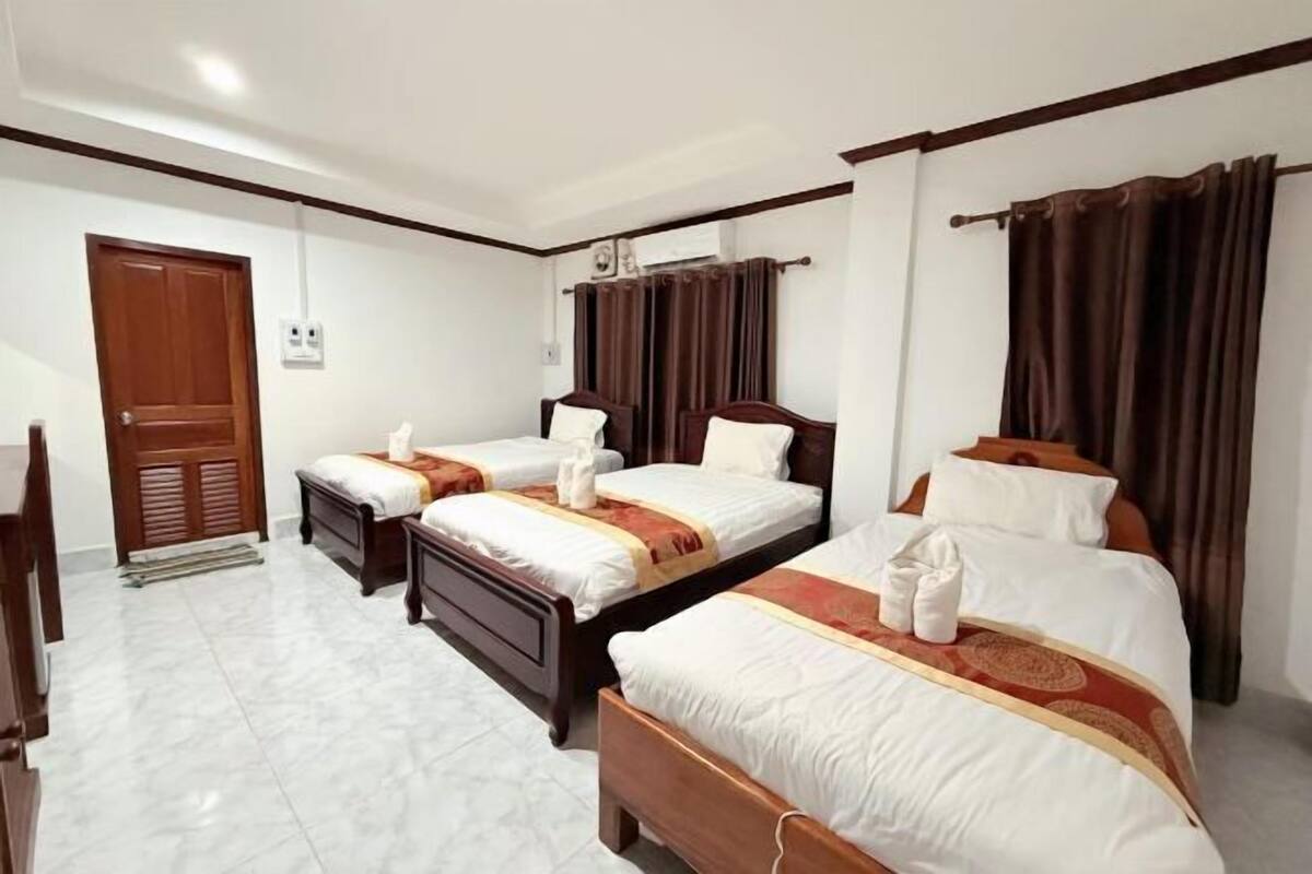 A hotel room with three beds, a wooden door, and a tiled floor.