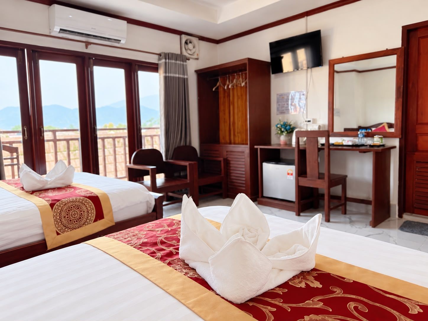 A hotel room with two beds, a desk, a chair, a television, and a view of the mountains.