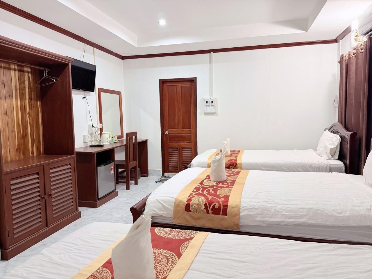 A hotel room with two beds, a desk, a wardrobe, and a mirror.