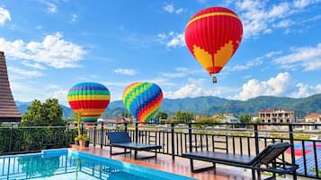 A pool area with lounge chairs and hot air balloons in the background.