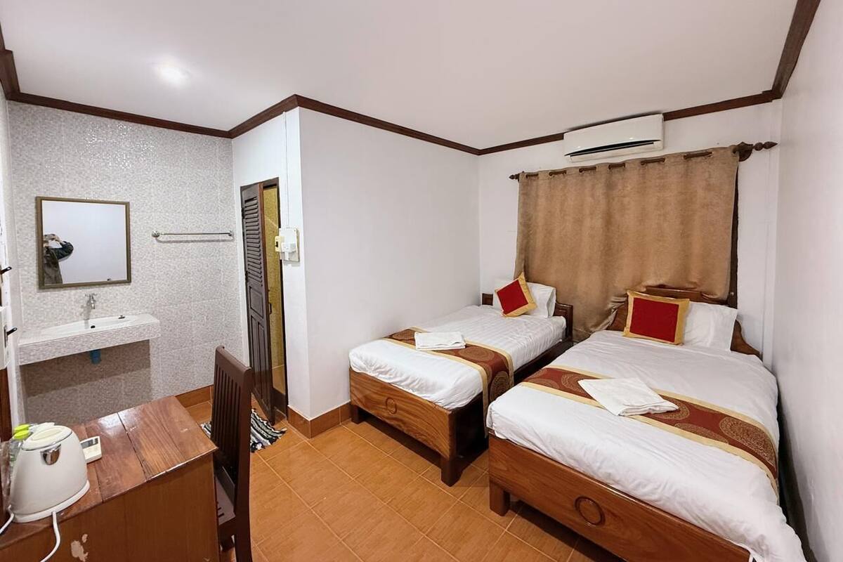 A hotel room with two beds, a desk, a sink, and an air conditioning unit.