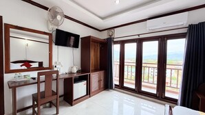 Une chambre d’hôtel équipée d’un bureau, d’une chaise, d’une télévision, d’une armoire et d’un balcon avec vue.