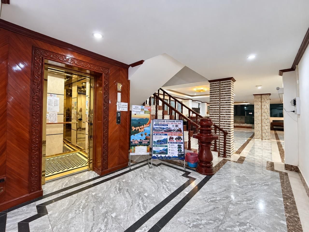 Un vestíbulo de hotel con suelo de mármol, una recepción de madera y una escalera.