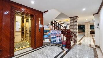Un vestíbulo de hotel con suelo de mármol, una recepción de madera y una escalera.