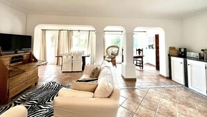A spacious living room with a sofa, a television, and a dining area with a table and chairs. - Inmitten Eines Mediteranen Gartens, Terrassiert, Befindet Sich das Appartment (Santa Eulària des Riu)