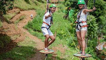 Dos personas en un circuito de tirolesa, usando cascos y arneses, con un área boscosa de fondo.