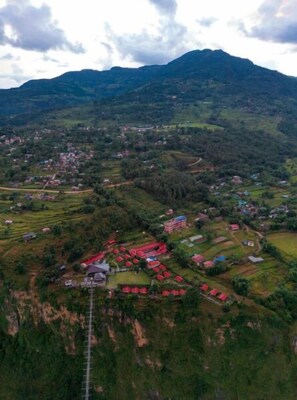 An aerial view of a rural village with terraced fields, scattered houses, and a prominent mountain range in the background.