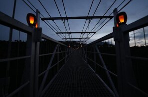A pedestrian bridge at dusk with metal railings and overhead cables.