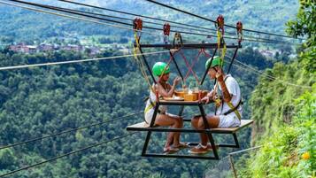 Two people on a suspended platform with a table, overlooking a forested valley.