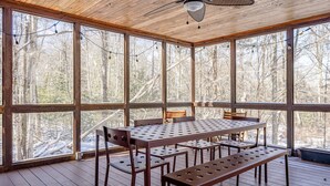A covered outdoor dining area with a table and benches, large windows, and a ceiling fan. - Charming & Cozy Cabin w/ Screened Porch (Stone Ridge)
