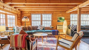 A log cabin interior with a sofa set, a rocking chair, a coffee table, and a patterned rug. - Charming & Cozy Cabin w/ Screened Porch (Stone Ridge)