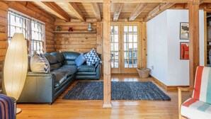 A cozy log cabin interior with a leather sofa, a woven floor lamp, and a wooden ceiling. - Charming & Cozy Cabin w/ Screened Porch (Stone Ridge)