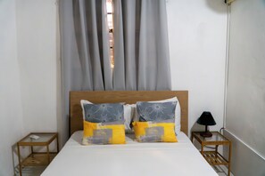 Un lit avec deux oreillers, une tête de lit en bois, une table de chevet avec une lampe et une fenêtre avec des rideaux.