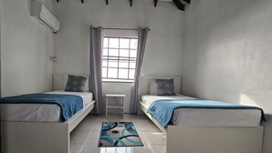 Una habitación con dos camas, una ventana con cortinas, una mesita y un equipo de aire acondicionado.