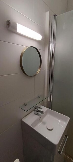 A bathroom with a round mirror, a sink, and a glass shower enclosure.