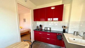 A compact kitchen with red cabinets, a wooden table, and a white sink. - Studio Tout Confort Giena-sils (Caen)