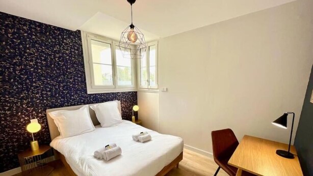 Hotellihuone, jossa on sänky, työpöytä, tuoli, ikkuna ja seinä, jossa on lehtikuvio.