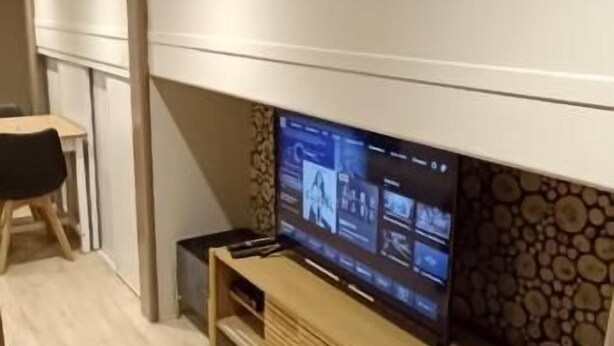 A modern living room with a flat-screen TV on a wooden stand, a stone wall, and a light-colored floor. - Appartement Antarès-sils (CAEN)