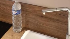 A kitchen with white shelves holding bowls and plates. A water bottle is on the counter. - Appartement Antarès-sils (CAEN)
