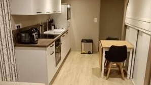 A compact living space with a kitchenette, a small dining table, a sofa, and a coffee table. - Appartement Antarès-sils (CAEN)