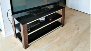 A flat-screen TV on a wooden stand with a shelf below. - Studio Lumineux Khara-sils (Caen)
