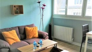A modern living room with a grey sofa, orange cushions, a wooden coffee table, and a radiator. - Studio Lumineux Khara-sils (Caen)