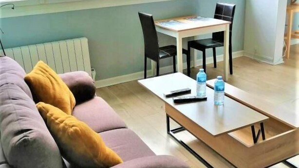A modern living room with a sofa, a coffee table, and a dining area with chairs. - Studio Lumineux Khara-sils (Caen)