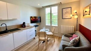 A compact living space with a kitchenette, a dining area, and a seating area with a sofa and chairs. - Grand Logement Jupiter-sils (CAEN)