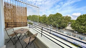 A balcony with a view of a street, a wooden table and chairs, and a bamboo screen. - Grand Logement Jupiter-sils (CAEN)