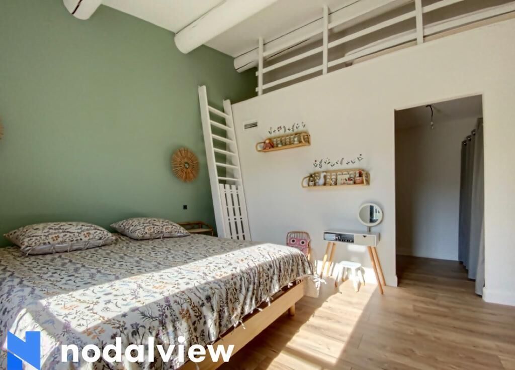 Een slaapkamer met een bed, een ladder, een bureau en planken met spullen aan de muur.