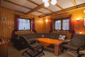 A cozy room with wooden walls, a bench, two chairs, a table with a tablecloth, and a lamp.