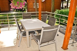 A table and chairs set outdoors with a metal railing, surrounded by greenery and a wooden building. - Four -anniversary Type C (Dzwirzyno)