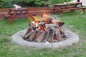 A fire pit with logs, surrounded by a stone border, and a wooden picnic table in the background. - Four -anniversary Type C (Dzwirzyno)