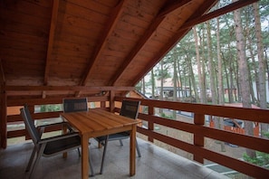 A wooden deck with a table and chairs, surrounded by a wooden railing, overlooking a forested area.