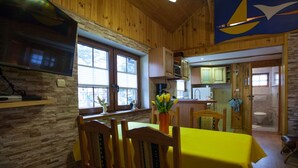 A wooden interior with a dining area featuring a yellow table and chairs, a kitchen with wooden cabinets, and a large window providing natural light. - Four -anniversary Type B (Dzwirzyno)